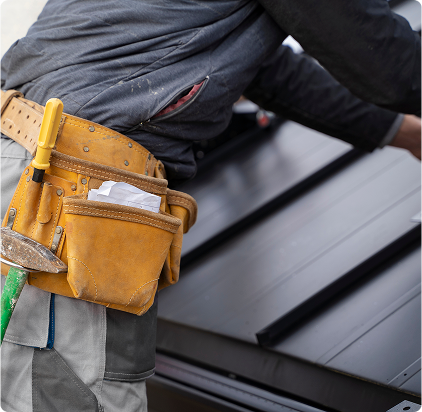 Roofing contractor with tool belt on roof, installing shingles or repairing damaged roof.