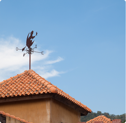 Weather vane on clay tile roof pointing north against blue sky background
